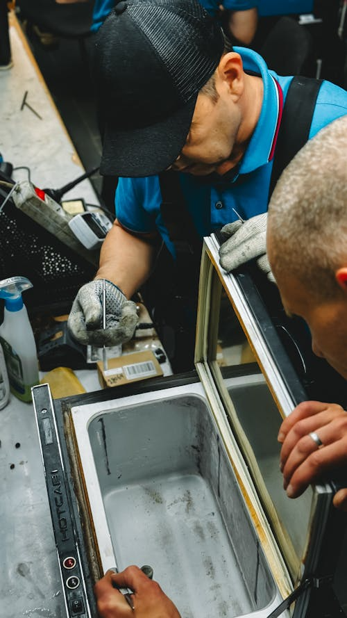 Two workers wearing gloves carefully repair or assemble a window frame in a workshop setting.